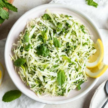 close up overhead photo of Lebanese slaw, Malfouf salad, in a pale pink bowl served with lemon wedges and fresh mint leaves