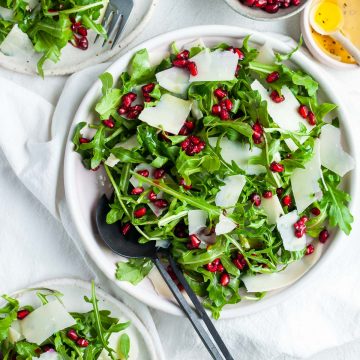 Rocket and pomegranate salad in a serving bowl, plates of the rocket salad just visible
