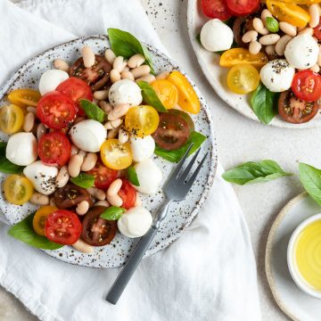 overhead photo of two plates of white bean caprese salad, with extra dressing on the side.