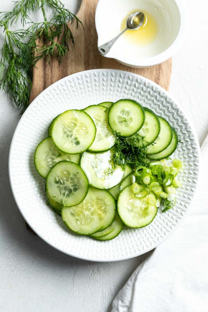 The sliced cucumber on a plate with the fresh dill and dressing just poured over it.