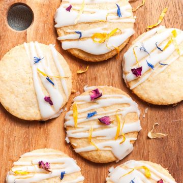 overhead photo of iced biscuits decorated with edible flowers on a wooden board
