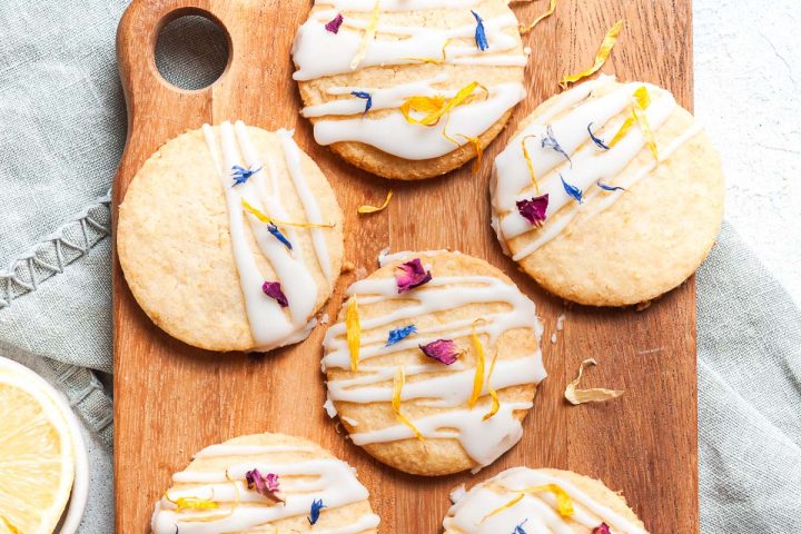 overhead photo of iced lemon biscuits decorated with edible flowers on a wooden board