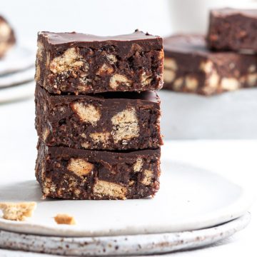 side view of a stack of three squares of chocolate hedgehog slice, to show the crushed biscuit base and melted chocolate top layer