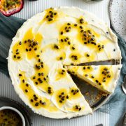 overhead photo of passionfruit cheesecake with a slice taken out and on a plate to the right of the cheesecake, extra passionfruit coulis to the side