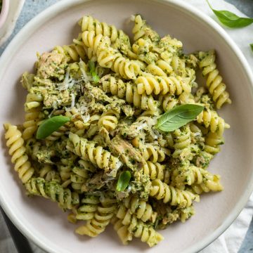overhead photo of tuna pesto pasta in a pale pink bowl scattered with fresh basil and black pepper, ready to eat