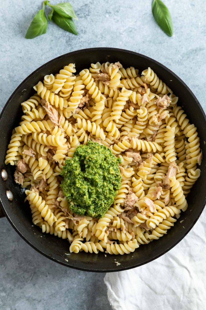 pan of tuna and cooked pasta, with a spoonful of pesto about to be mixed in.