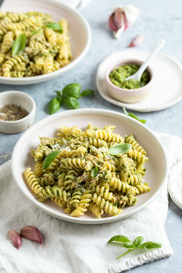 side view of two bowls of pasta ready to be served, a small bowl of extra basil pesto on the side