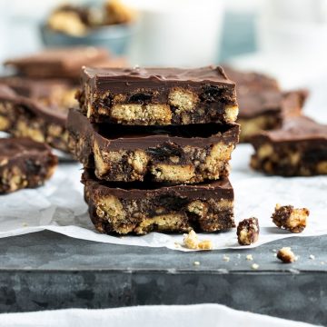 three squares of chocolate tiffin stacked one on top of another to show the crunchy biscuit and sultana layer and melted chocolate top