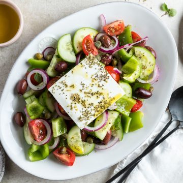 Greek peasant salad on a serving platter, with extra capers and olive oil in dishes to the side