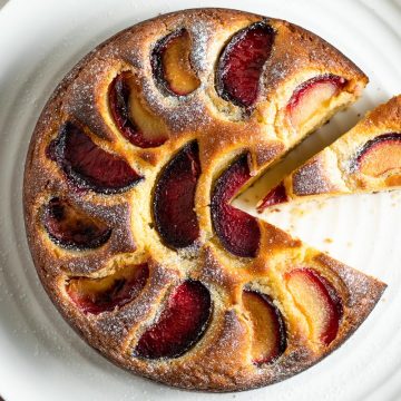 overhead photo of yogurt plum cake on white plate to show plum pattern on the top of the cake