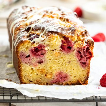 a close up of a cut raspberry and white chocolate loaf cake to show the even distribution of raspberries and fluffy texture of cake