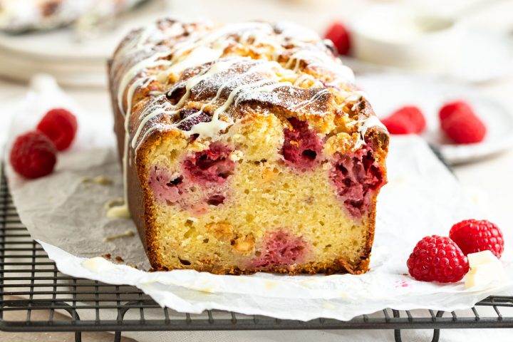 a close up of a cut raspberry and white chocolate loaf cake to show the even distribution of raspberries and fluffy texture of cake