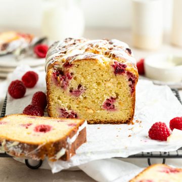 cut white chocolate and raspberry loaf cake to show the texture, fresh raspberries dotted around the cake