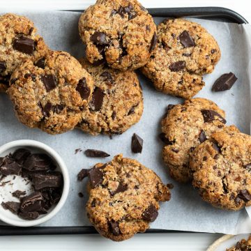 tray of almond chocolate chip cookies on a tray with extra chocolate chunks in a bowl on the side