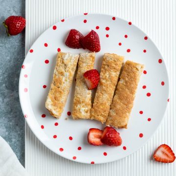baby eggy bread cut in to fingers and served with fresh strawberries on a red spotted plate