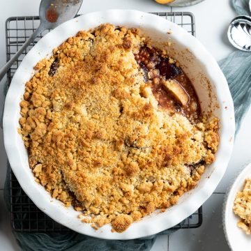 plum and apple crumble in white pie dish, a portion taken out and served in a bowl just visible to the right
