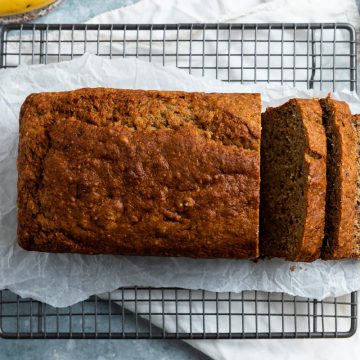 overhead photo of a loaf of buckwheat banana bread on a cooling rack, some slices sliced off to the right