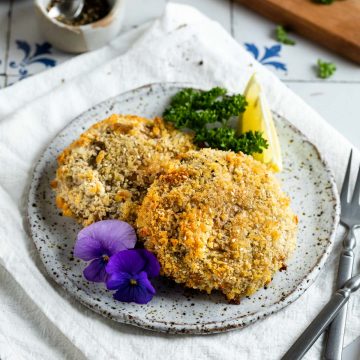 two mushroom schnitzels on a plate served with parsley and a lemon wedge