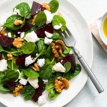 a plate of beetroot walnut and feta salad with a bowl of extra orange dressing to the right of the plate
