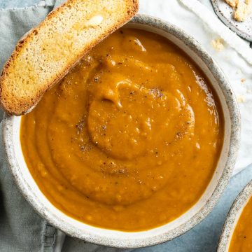 a bowl of roast pumpkin soup with a slice of buttered toast on the edge of the bowl ready to dip in to the soup