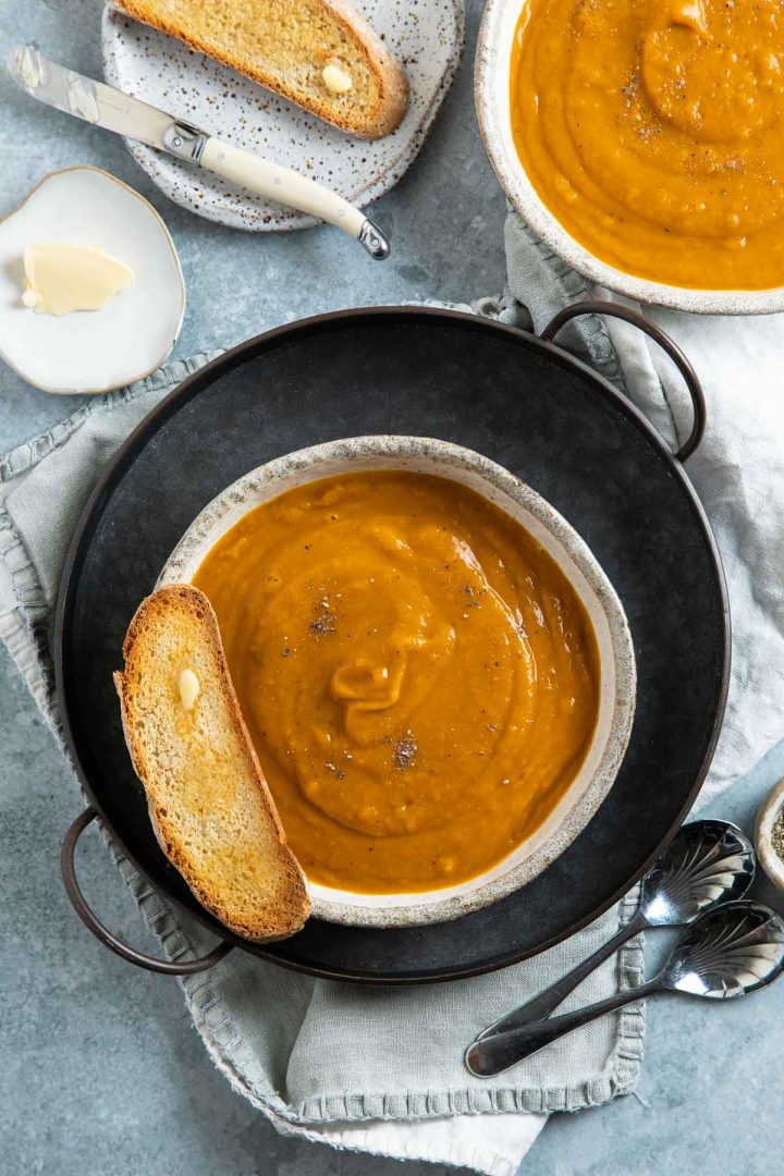 a bowl of soup on a metal tray with a slice of buttered toast on the left edge of the bowl
