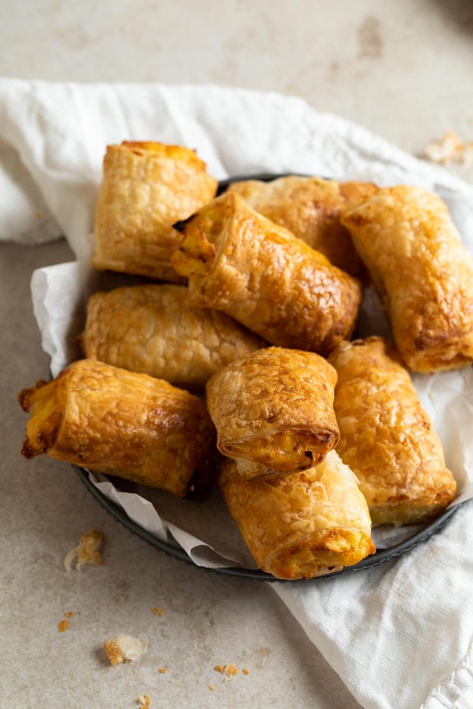 A pile of cooked golden puff pastry rolls on white tea towel on a metal plate
