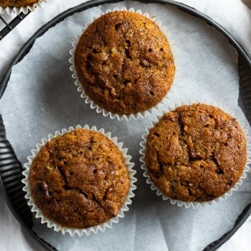 three freshly baked pumpkin muffins on some white baking paper on a round plate