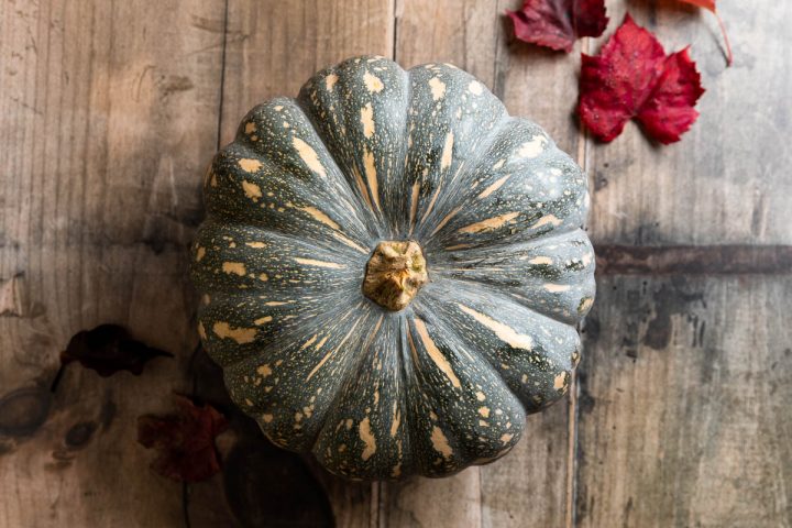 a seasonal whole pumpkin on a wooden background with red Autumnal / fall leaves