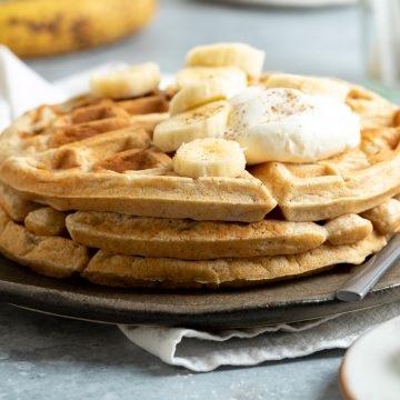 side view of a stack of three banana waffles on a plate topped with Greek yogurt and sliced banana