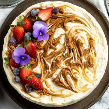 Overhead view of Biscoff cheesecake to show the marbled Biscoff decoration and the topping of berries and purple edible flowers