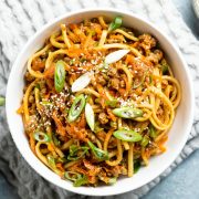 hoisin beef noodles served in a white bowl sprinkled with sliced spring onions and sesame seeds
