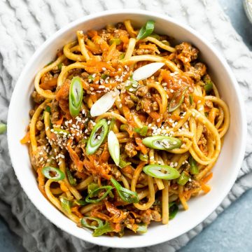 hoisin beef noodles served in a white bowl sprinkled with sliced spring onions and sesame seeds