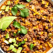 Close up of Mexican beef mince in a blue pan, topped with fresh coriander and avocado cubes.