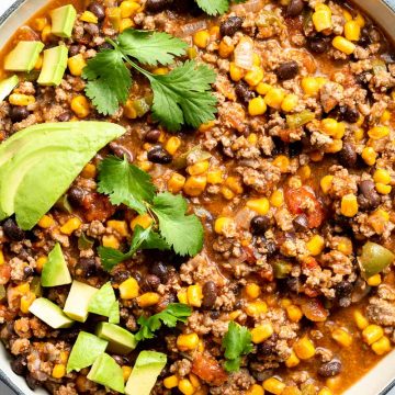 Close up of Mexican beef mince in a blue pan, topped with fresh coriander and avocado cubes.