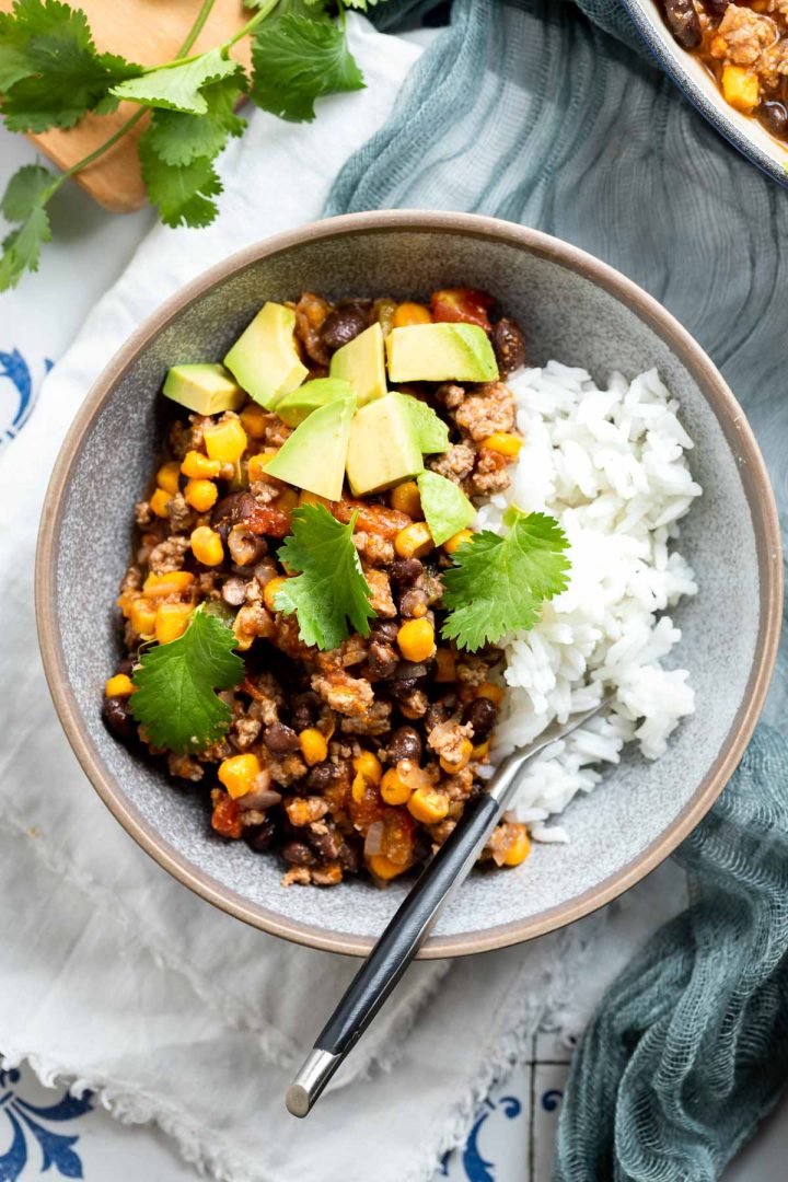 A blue bowl filled with Mexican mince and rice ready to eat, topped with avocado cubes