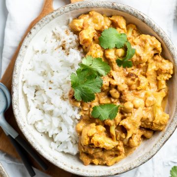 cauliflower chickpea curry served in a light coloured bowl with steamed rice, sprinkled with fresh coriander leaves