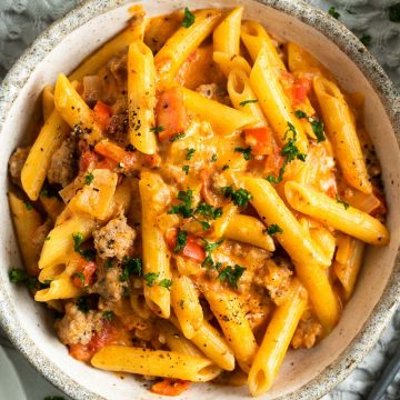 a bowl of one pot creamy sausage pasta with a fork next to eat ready to eat, a bowl of salad just visible in the top right corner