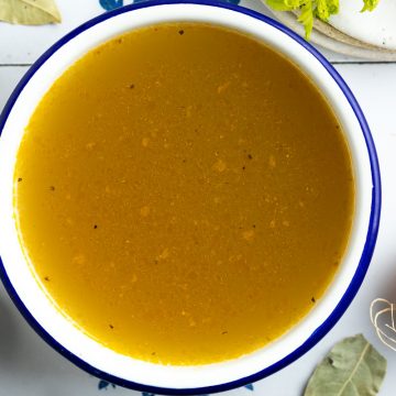 a bowl of homemade vegetable stock with onions and herbs dotted around the sides