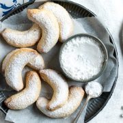 plate of vanillakipferl (Austrian crescent cookies) with bowl of icing sugar / confectioners sugar and spoon ready to dust the cookies.
