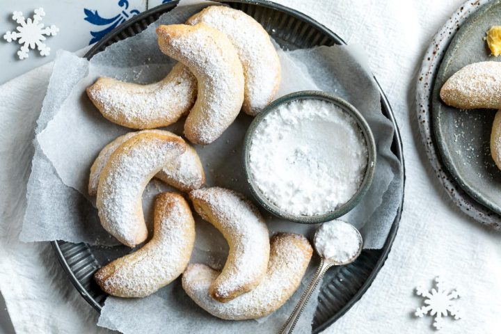 plate of vanillakipferl (Austrian crescent cookies) with bowl of icing sugar / confectioners sugar and spoon ready to dust the cookies.