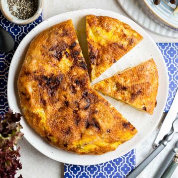 Spanish tortilla on a white plate with blue tiled background ready to serve with salad