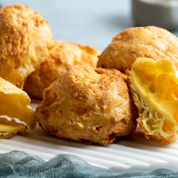 pile of gougeres on white plate, some cut open to show airy texture