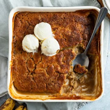 banana self saucing pudding in a white square baking dish serving with 3 scoops of vanilla ice cream