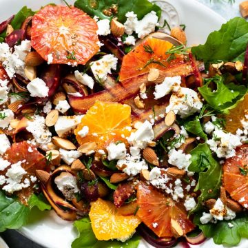 Carrot and orange salad on white serving platter sprinkled with feta, almonds and fresh herbs.