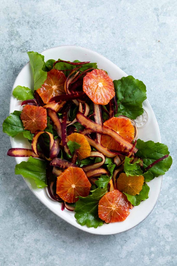 Blood orange slices and carrot ribbons placed over the rocket (arugula) leaves