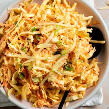 close up of cheese coleslaw in a bowl with a black serving spoon
