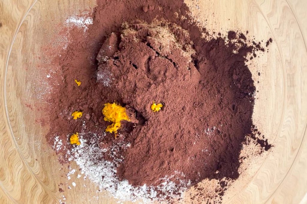 a glass bowl with flour, baking powder, baking soda,sugar, orange zest, cocoa powder