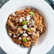 a white bowl of cooked Greek lamb shanks served topped with crumbled feta and fresh oregano