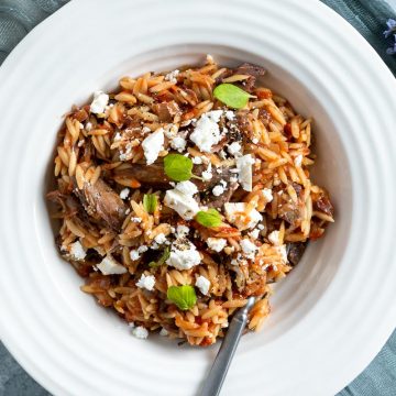 a white bowl of cooked Greek lamb shanks served topped with crumbled feta and fresh oregano