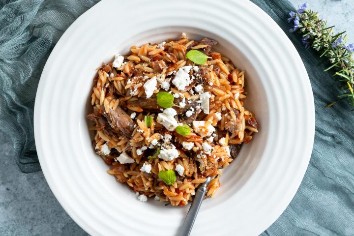 a white bowl of cooked Greek lamb shanks served topped with crumbled feta and fresh oregano